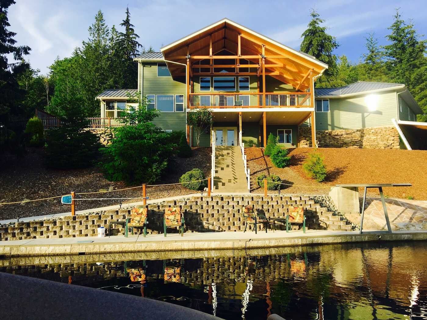 Large custom home with timber-frame gable above a block retaining wall and lake shore