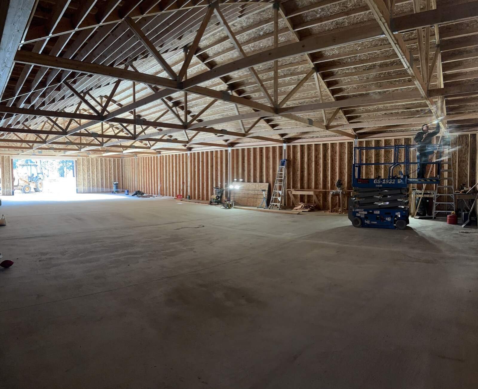 Inside a large pole building under construction with open trusses and a concrete floor