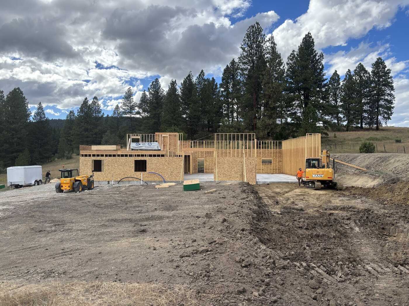 Excavated rural home site with an excavator, loader and new framing among ponderosa pines