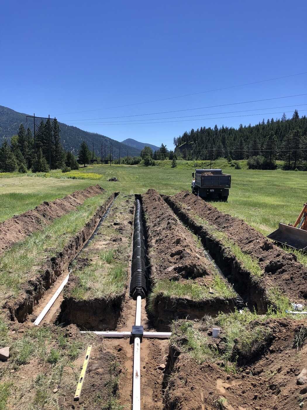 Open septic drain field trenches with distribution pipe in a mountain meadow