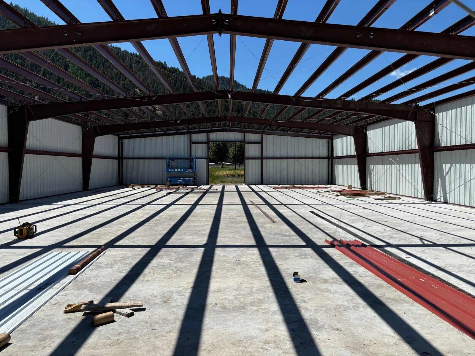 Steel building frame standing on a new concrete slab below forested mountains