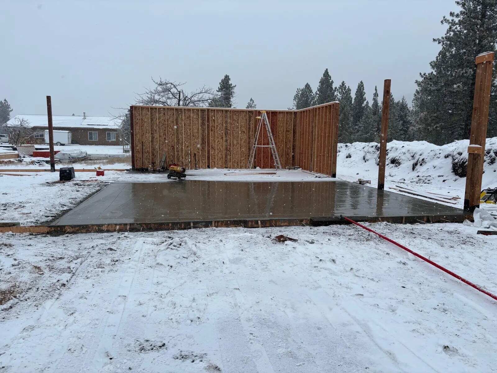 New concrete slab and first framed wall on a snowy western Montana lot